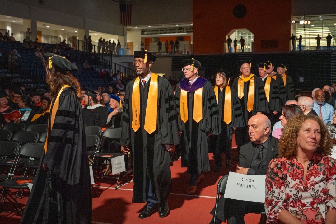 R I T Trustees in academic regalia with gold stoles process into the inauguration ceremony as guests look on.