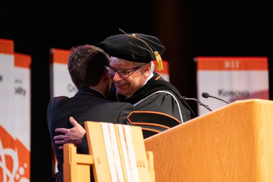 R I T President Sanders hugs a person on stage at the podium during the ceremony.