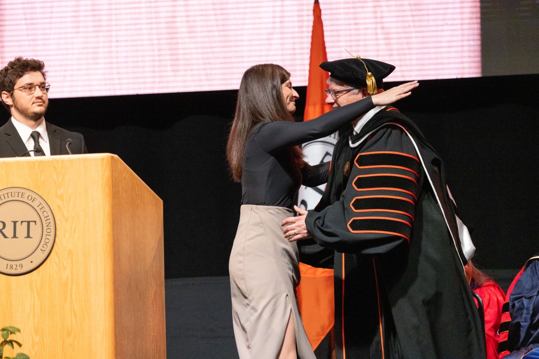 R I T President Sanders hugs his daughter on stage beside the RIT podium.