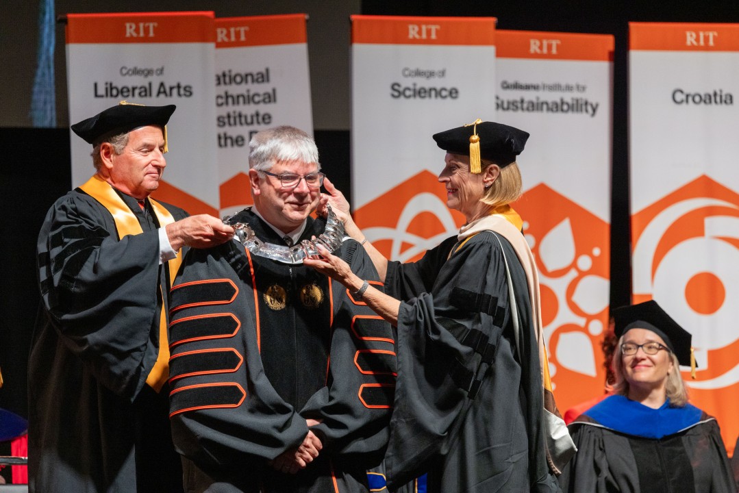 R I T President Sanders crouches down as two trustees place the presidential medallion collar around his neck.
