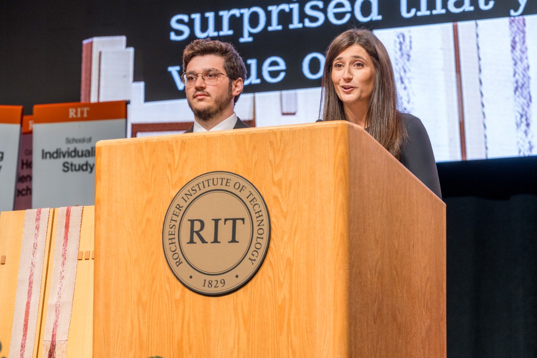 Two speakers stand at the R I T podium addressing the audience during the ceremony.
