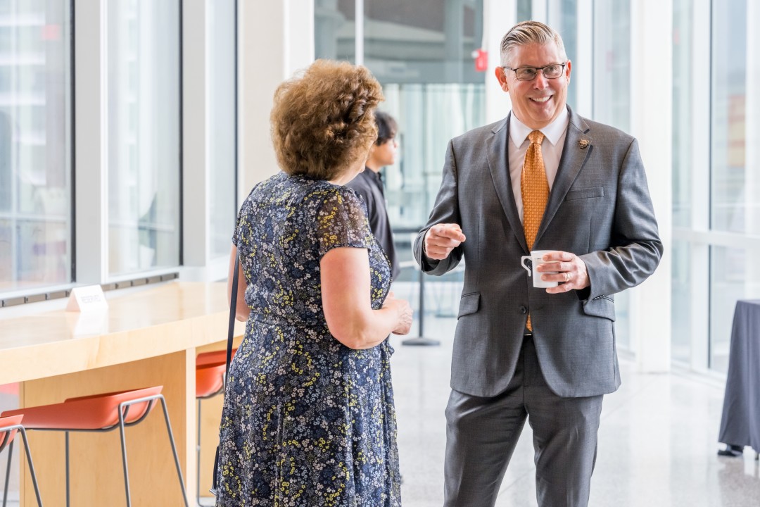 Ryne Raffaelle smiles and speaks to a woman.