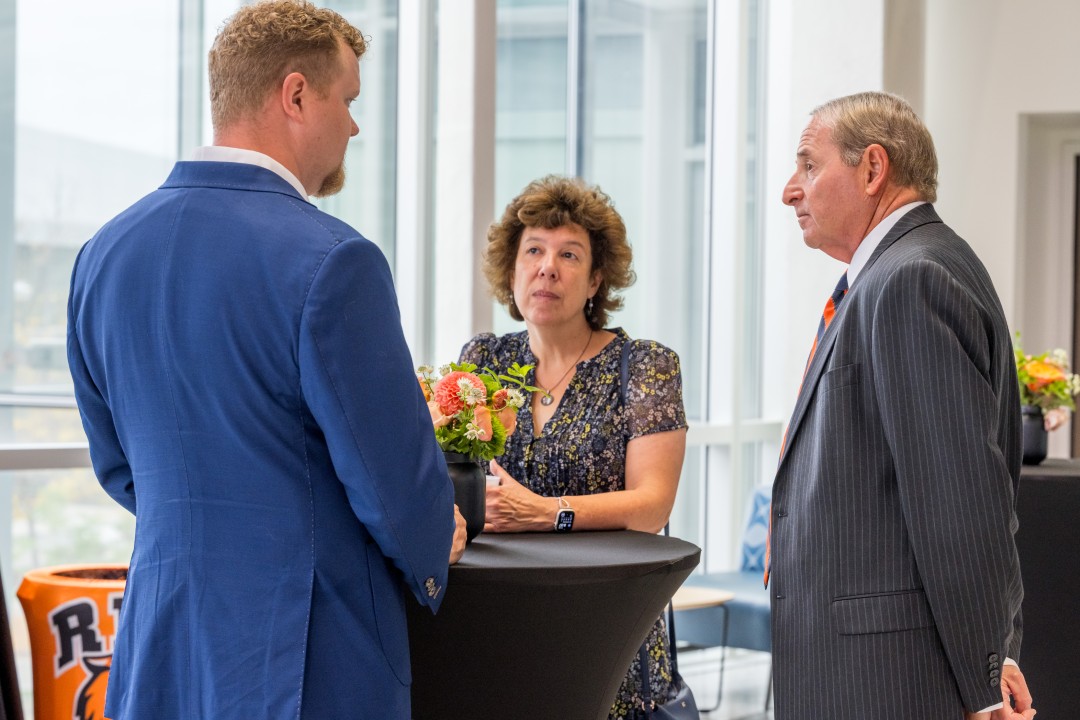 Three people stand chatting at a small table at a reception event.