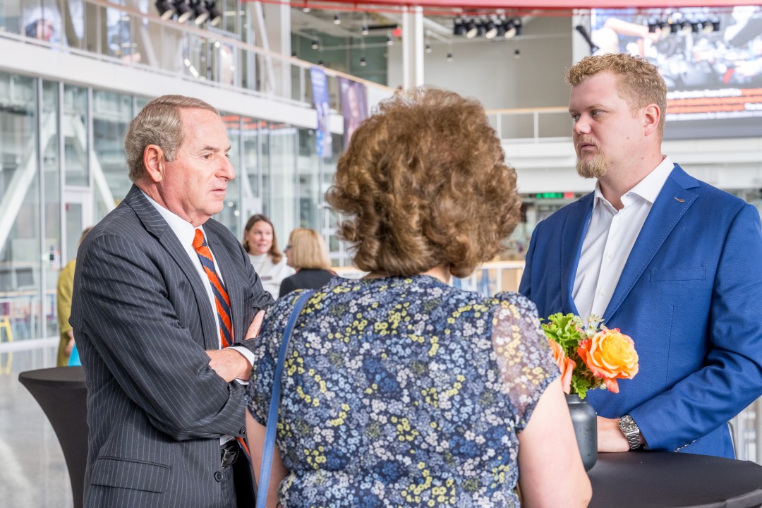 Three people stand chatting at a small table at a reception event.