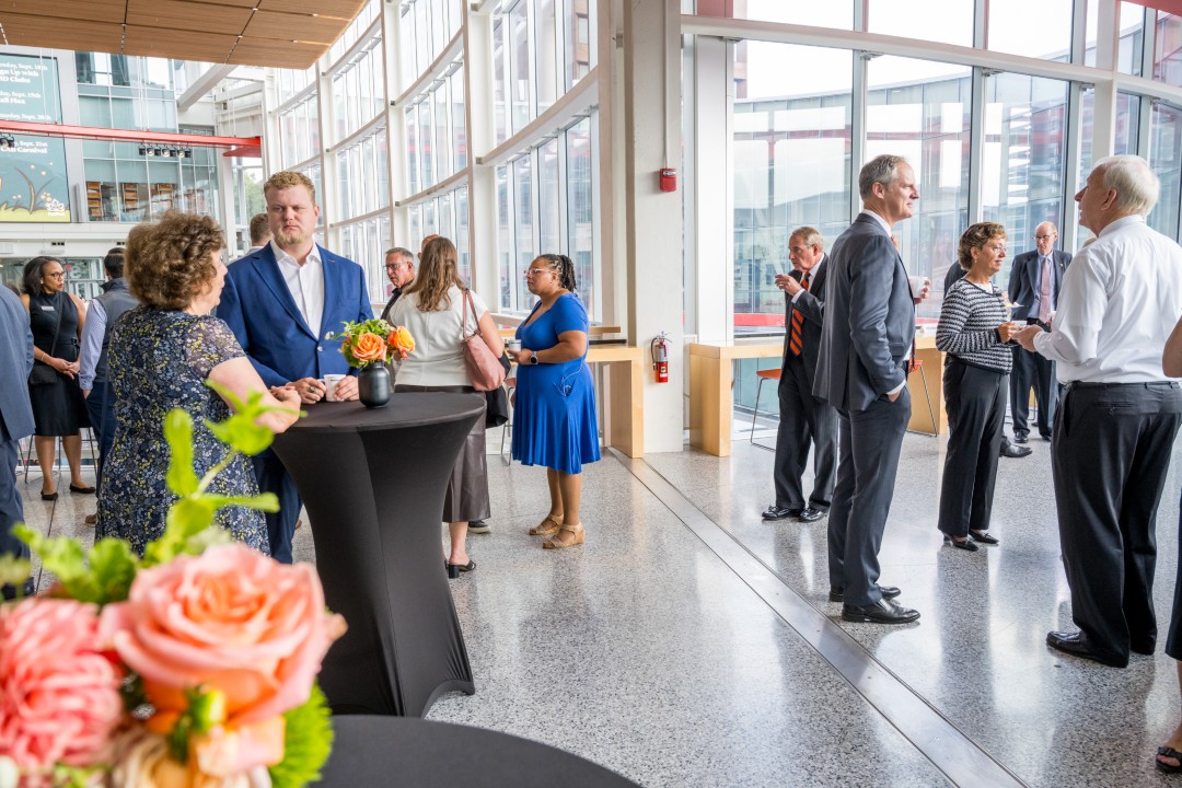 People standing and talking at a reception event in a brightly-lit atrium.