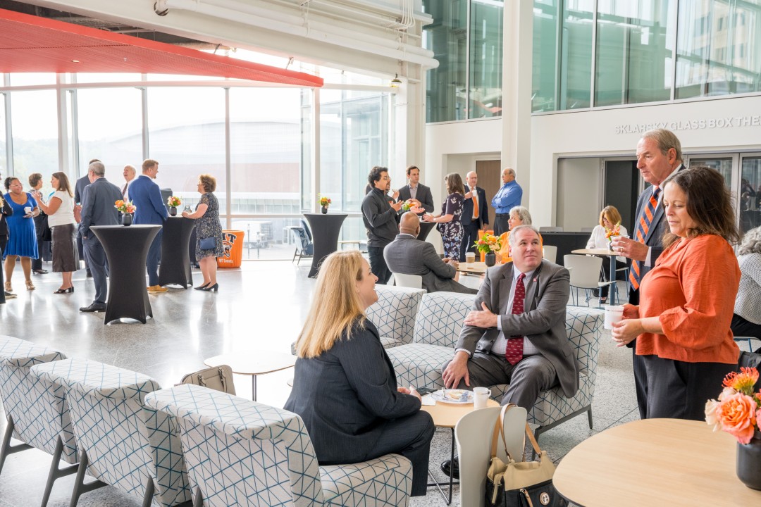 A wide view of a reception in a brightly lit atrium, with attendees talking while standing or seated.