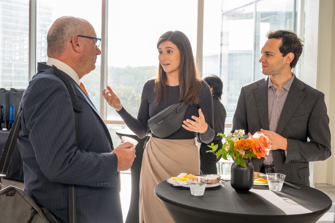 Three people talking while eating breakfast at a reception.