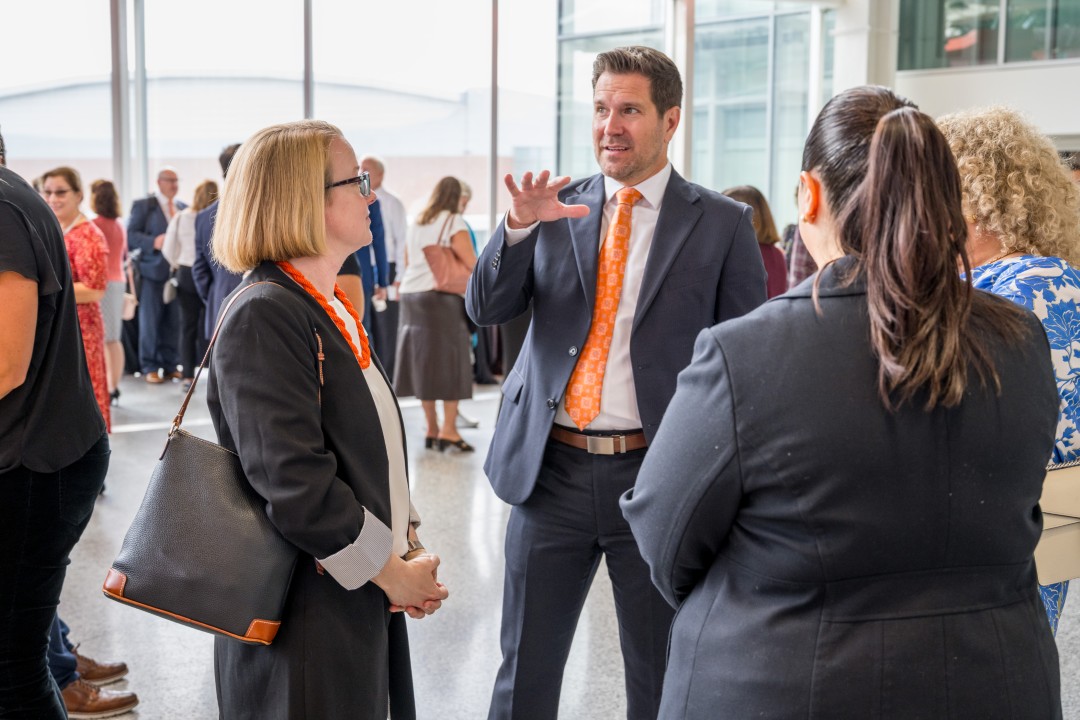 Three people listening to another speak at a reception event.