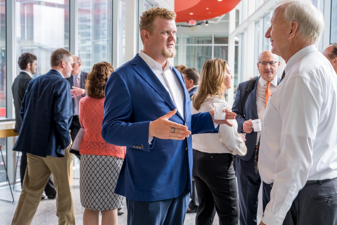 Two people talk in the foreground as other event attendees mingle in the background.