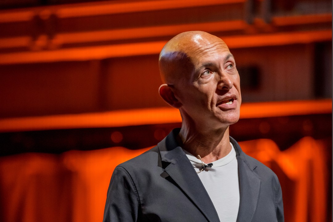 A man in a gray suit speaks at an event.