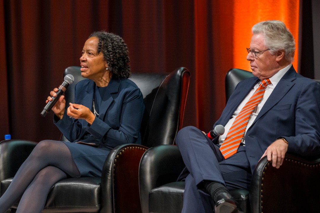 A woman speaking into a microphone as the man seated next to her listens.