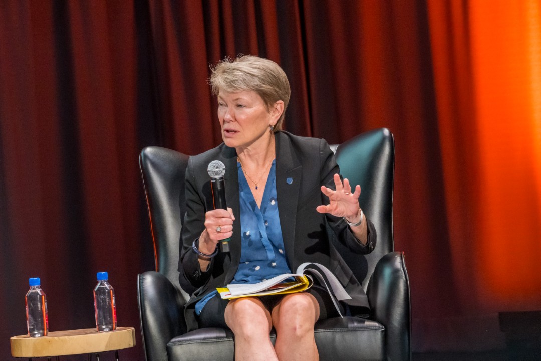 A seated woman speaking into a microphone as part of the panel.