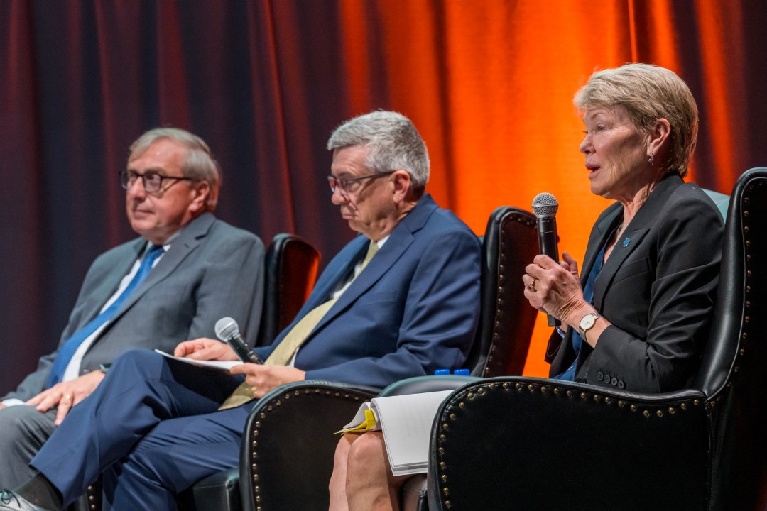 Three seated panelists, with one speaking into a microphone.