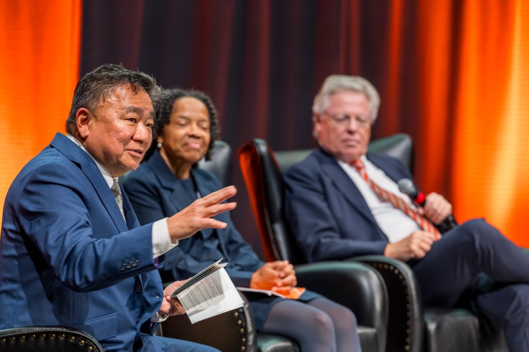 A panelist speaks as two others listen in the background.