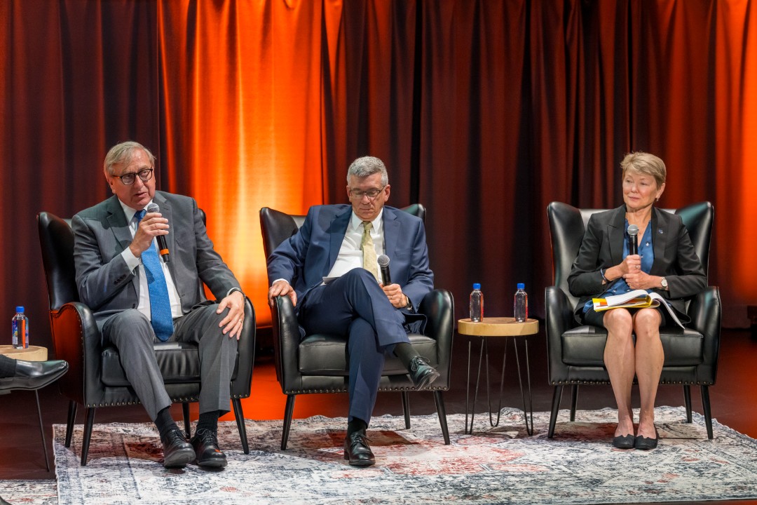 Three seated panelists, with one speaking into a microphone.