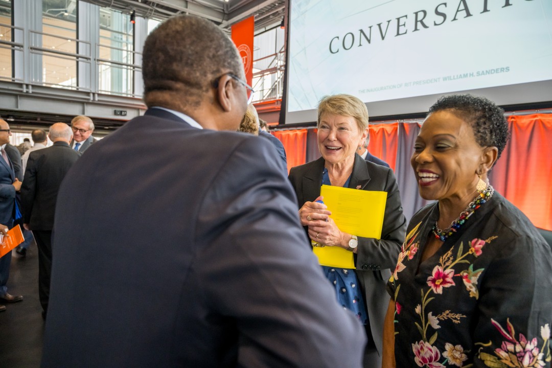 Three people standing while smiling and talking.