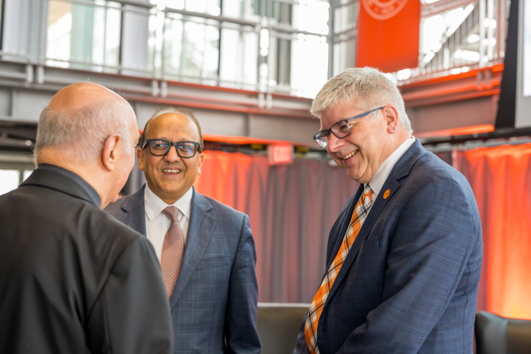 R I T president Sanders smiles and talks to two other people.