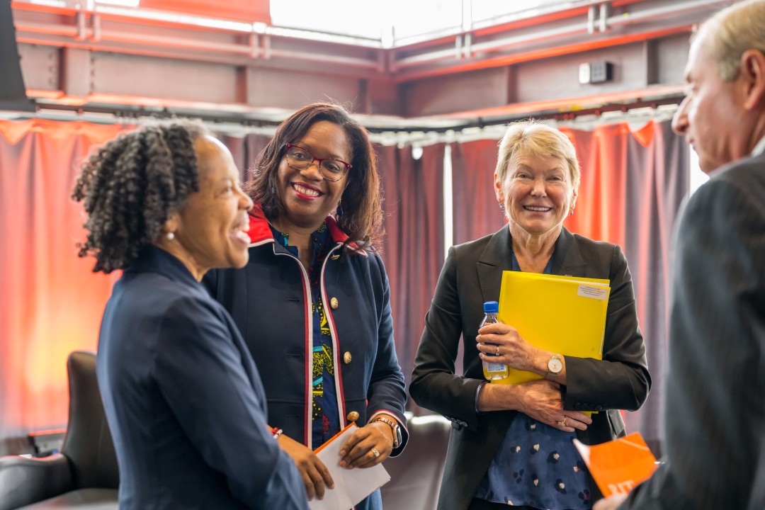 Four people standing, smiling and talking to one another.