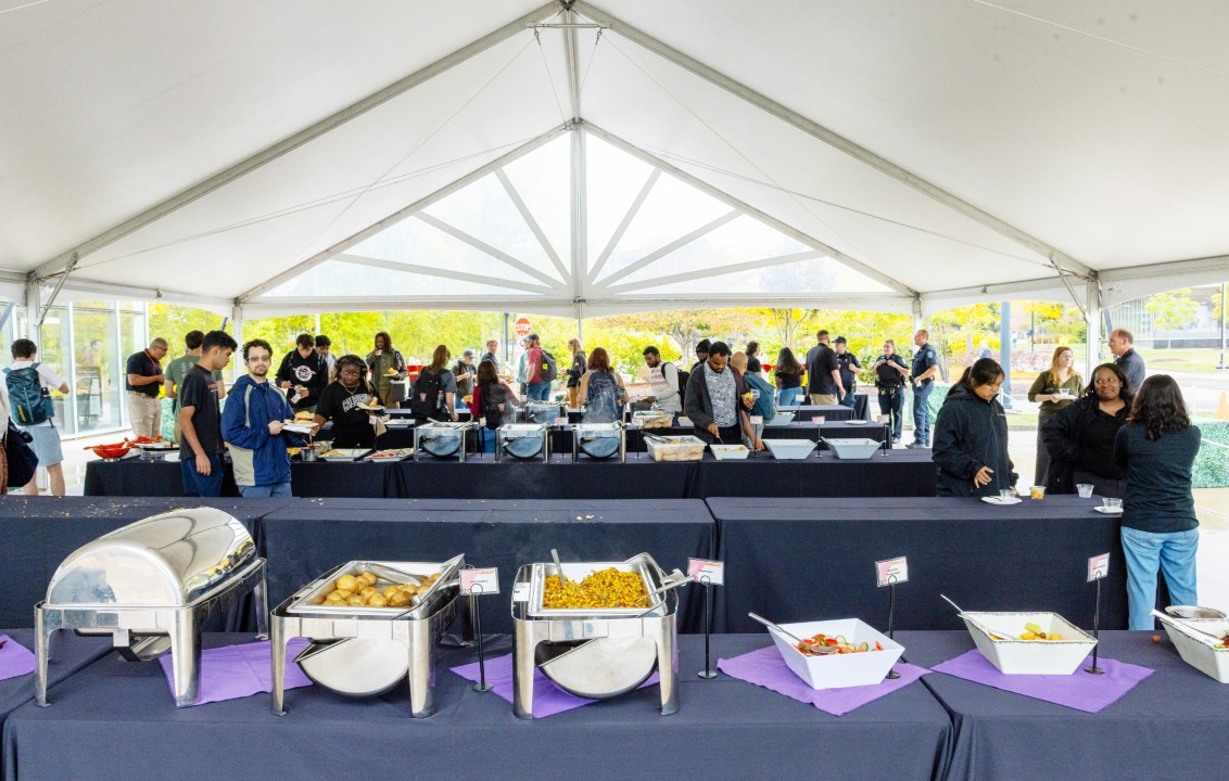 Guests line up at buffet tables under a large white tent filled with food trays.