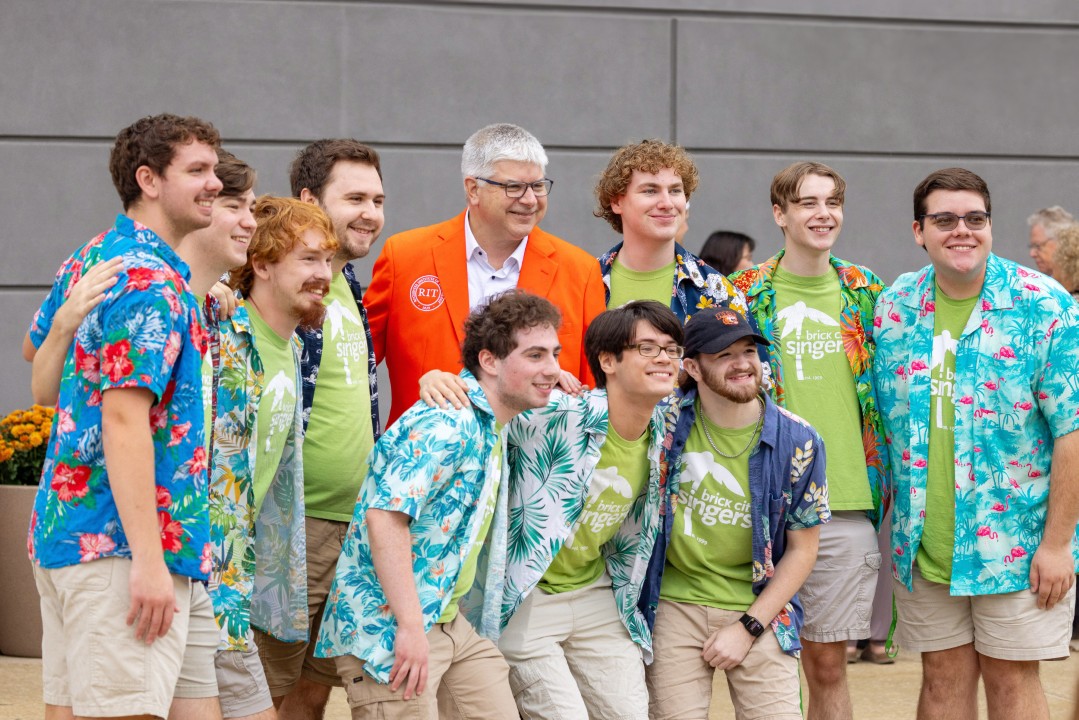 A group of students in matching performance shirts pose for a group photo with R I T president Sanders.