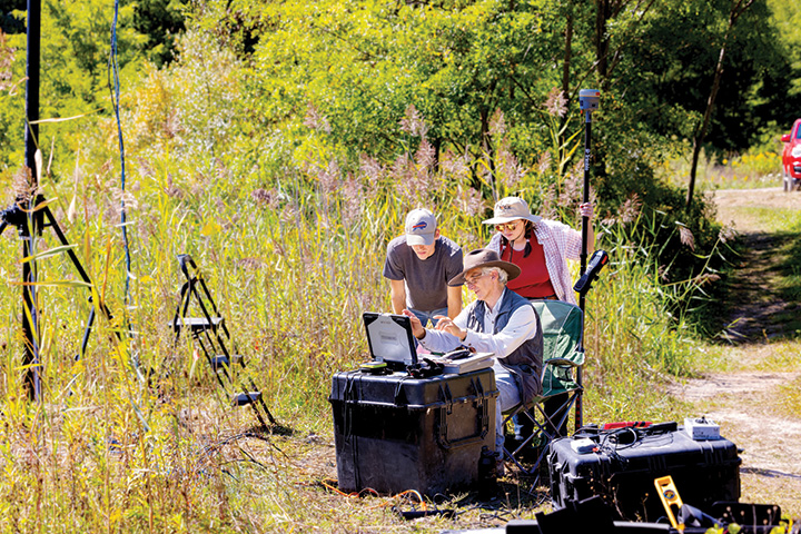 Researchers outside with measuring equipment, surrounded by tall grass.