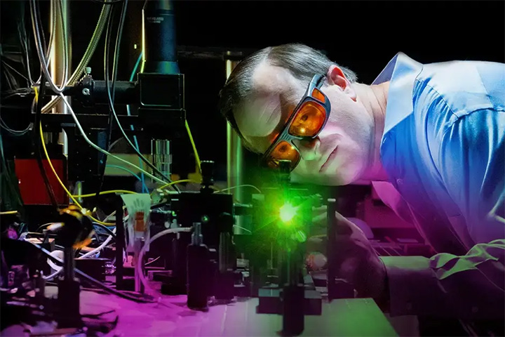 Researcher looking at a bright green light, like a laser.
