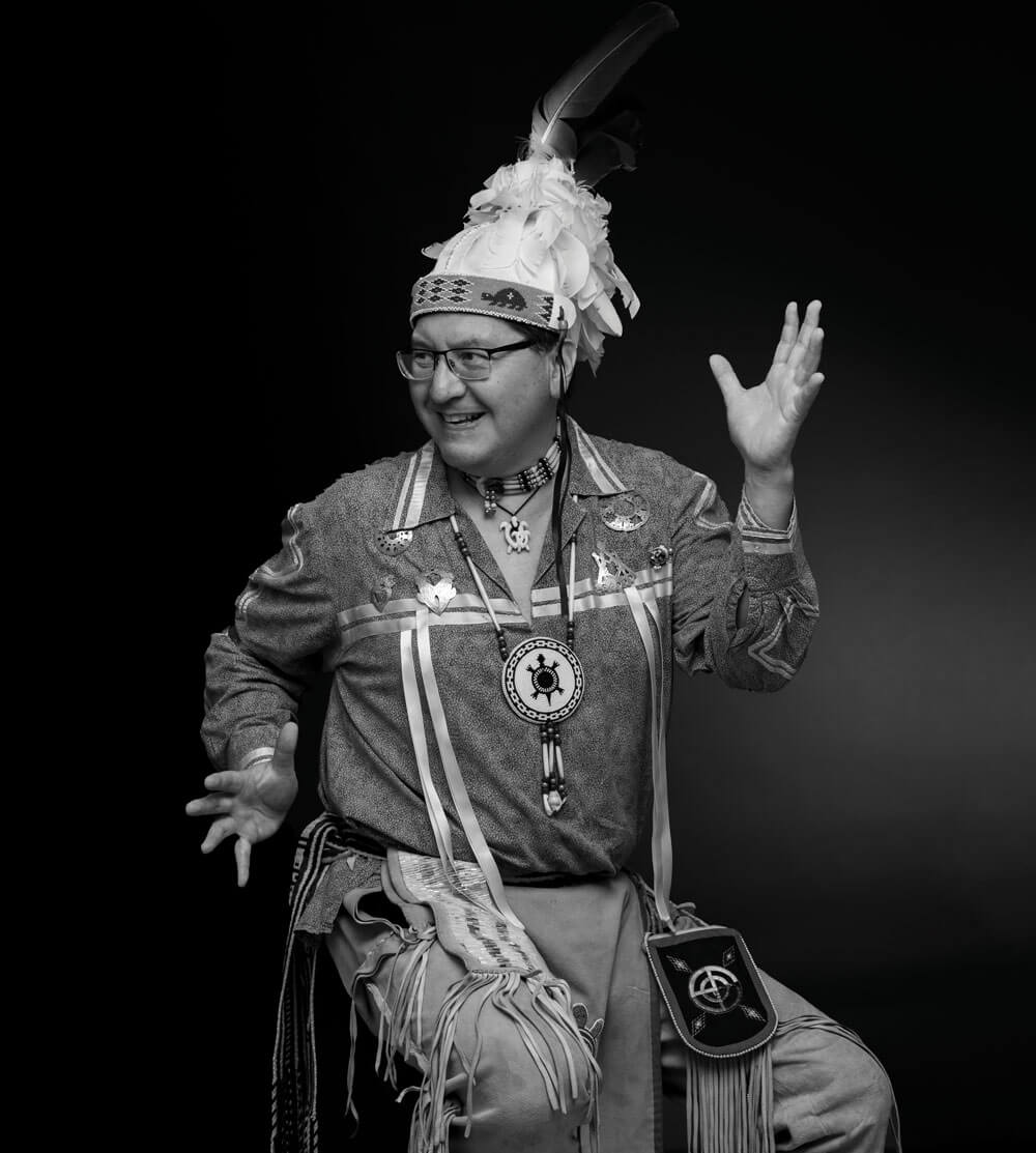 Perry Ground sitting on a stool, wearing traditional Native American apparel.