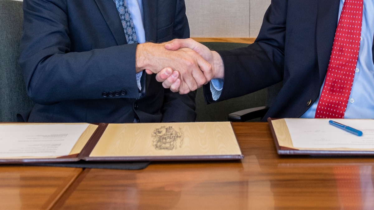 two people shaking hands over official documents on a desk.