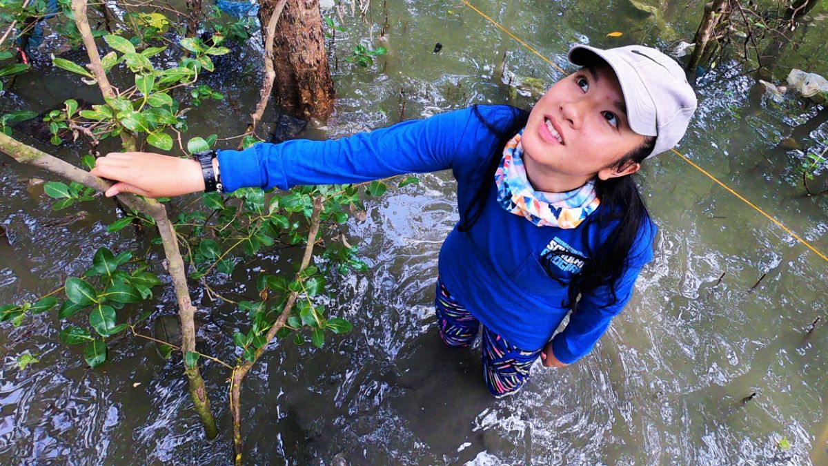 A person wearing outdoor gear, standing in a swampy forest, and conducting environmental fieldwork.