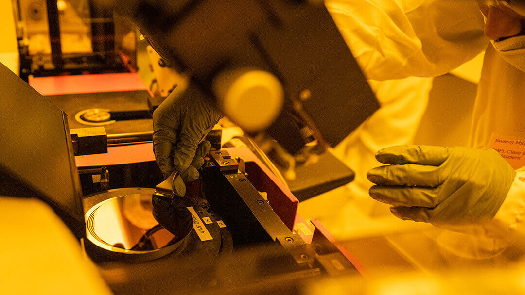 A close up of a person in a clean room picking up a semiconductor wafer.
