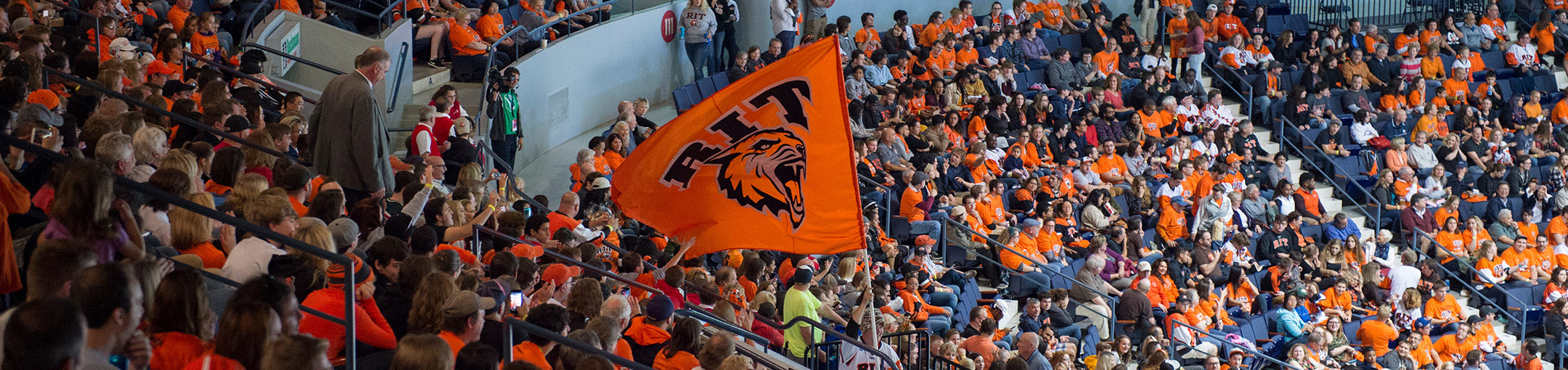 A student waving the RIT Tiger flag in the corner crew section at an RIT hockey game