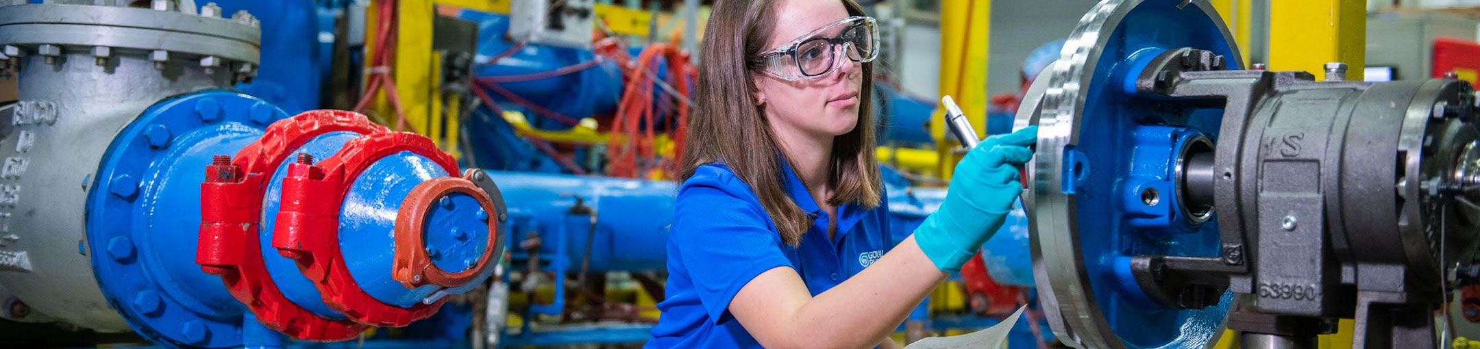 a woman with safety goggles working on large metal pipes