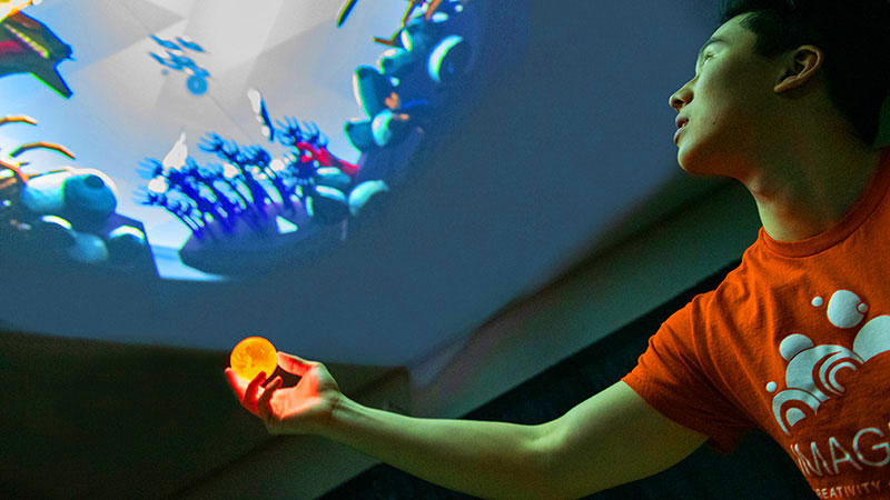 a student holding up a glowing orange ball beneath a projection