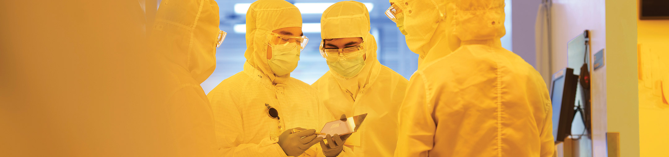 people wearing yellow clean suits looking at a semiconductor.