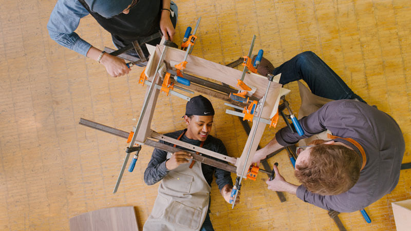 three students building a stand out of wood