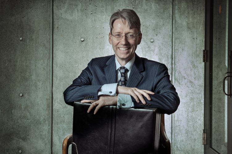 Clyde smiling in a chair holding a briefcase