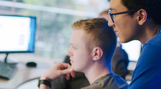 Two  people looking over the shoulder of someone at a laptop