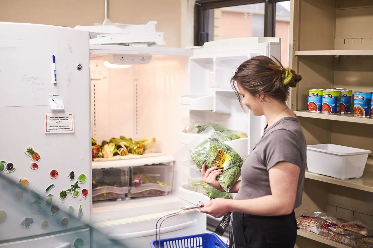 An R I T student standing in front of an open refrigerator, looking at a bag of greens.