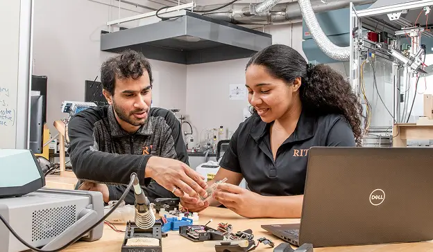 Two R I T students working with components at a soldering station.