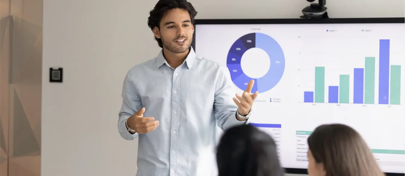 A person standing in front of a screen with graphs on it, giving a presentation.
