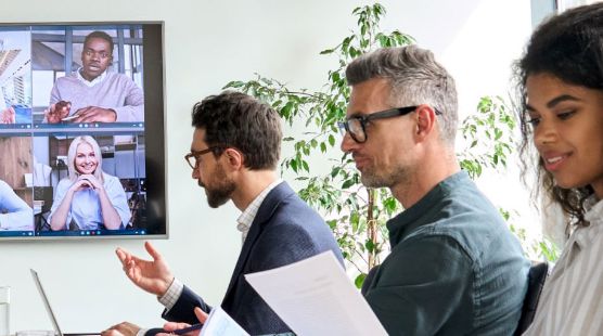 Three people sitting in a board room with a zoom call on the computer screen
