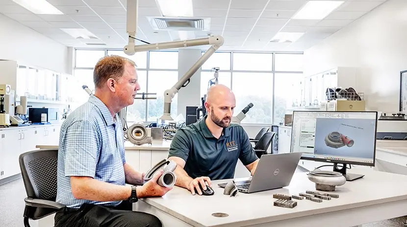 Two engineers sitting at a desk in front of a laptop and monitor.