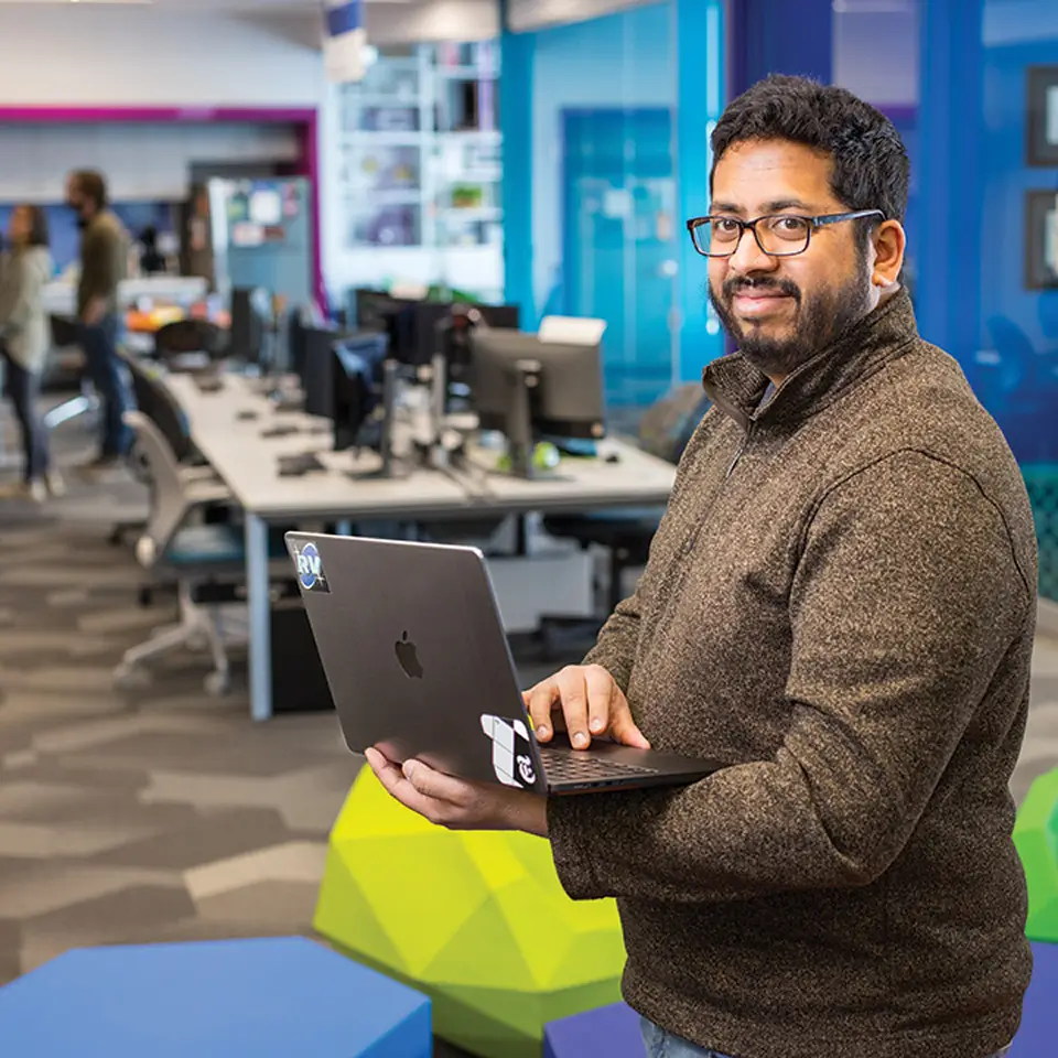Rohit Crasta poses for a photo while holding a laptop.