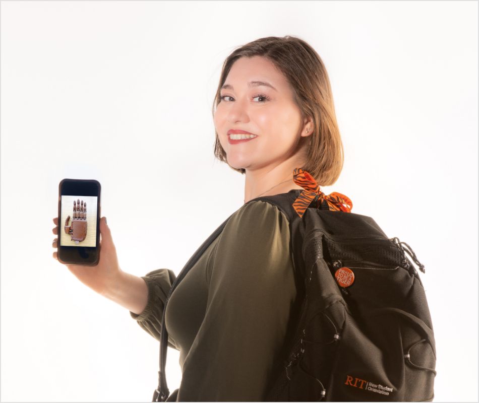 Maggie brooks smiling and showing off a picture of a prosthetic on her phone