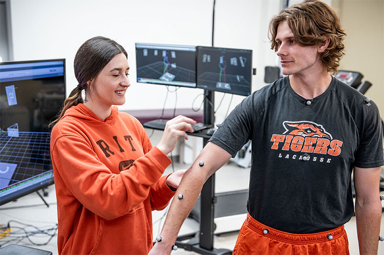 A female student placing sensors on a male students arm, waist, and neck.