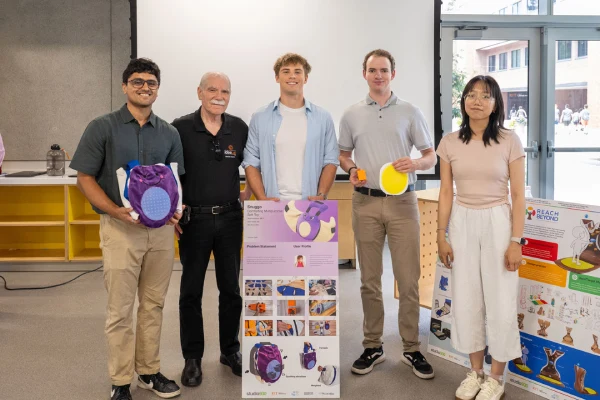 Members of a studio posing for a photo in a classroom