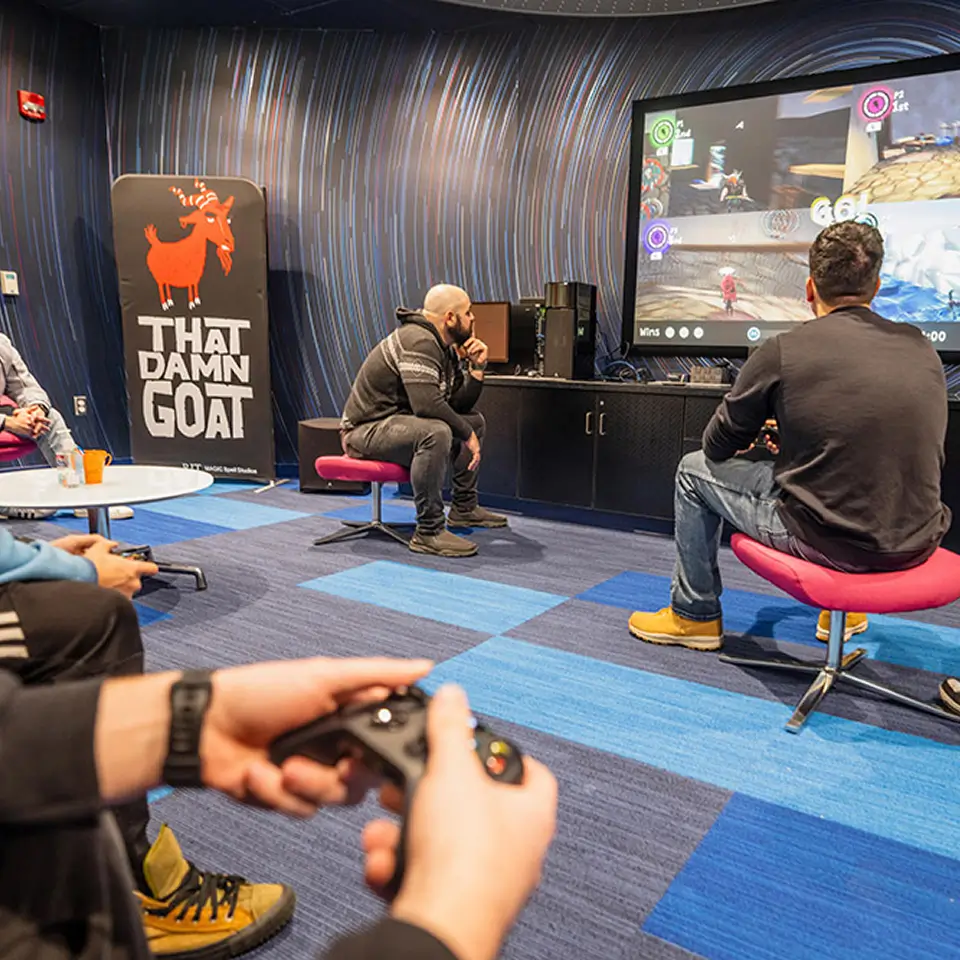 Four people gathered around a TV playing That Damn Goat.