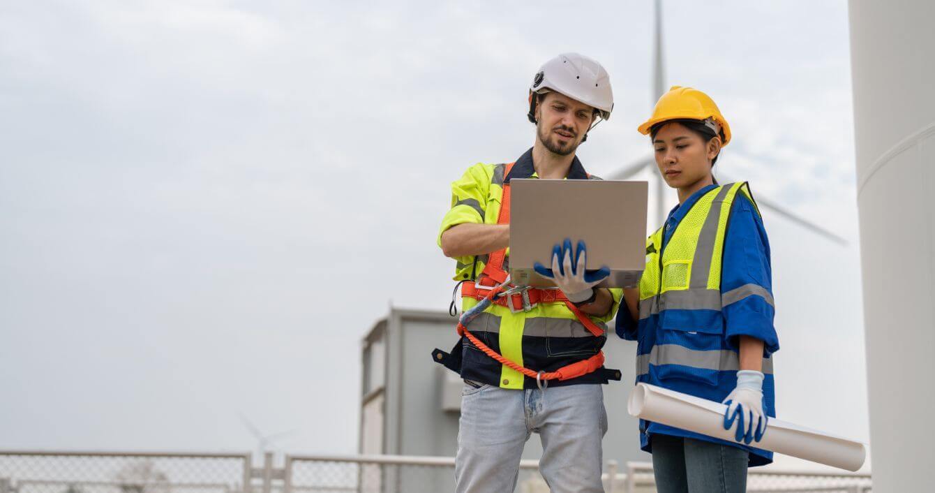 Two engineers outside with hard hats discussing something on a laptop