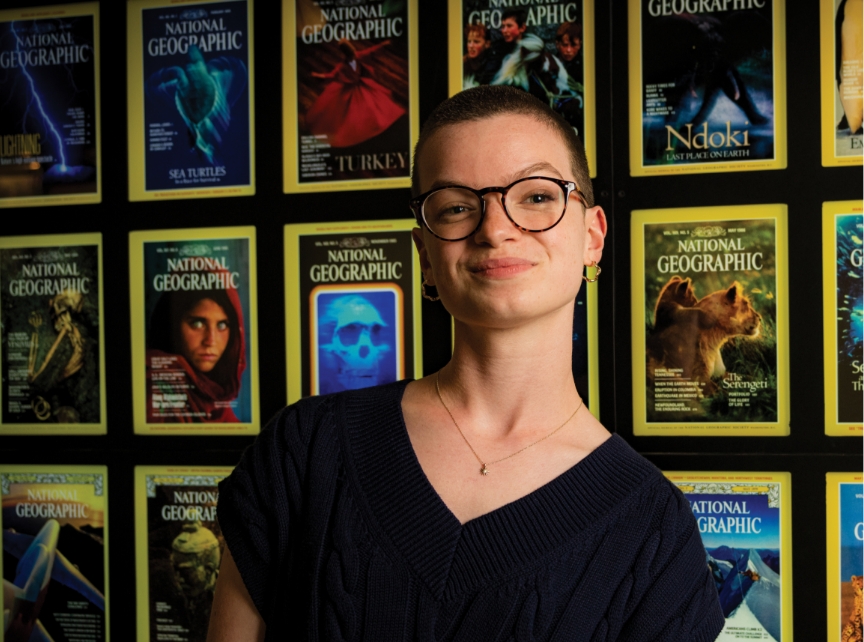 student posing in front of a wall filled with national geographic covers