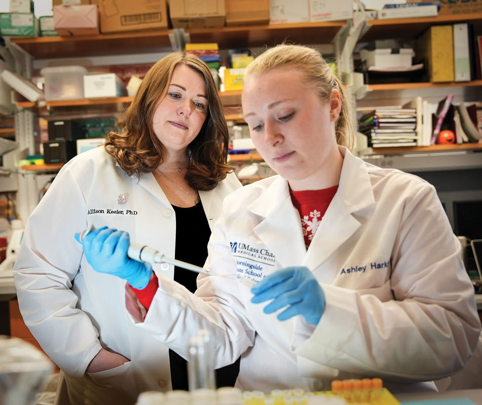 a student and professor are seen in lab coats using a pipette